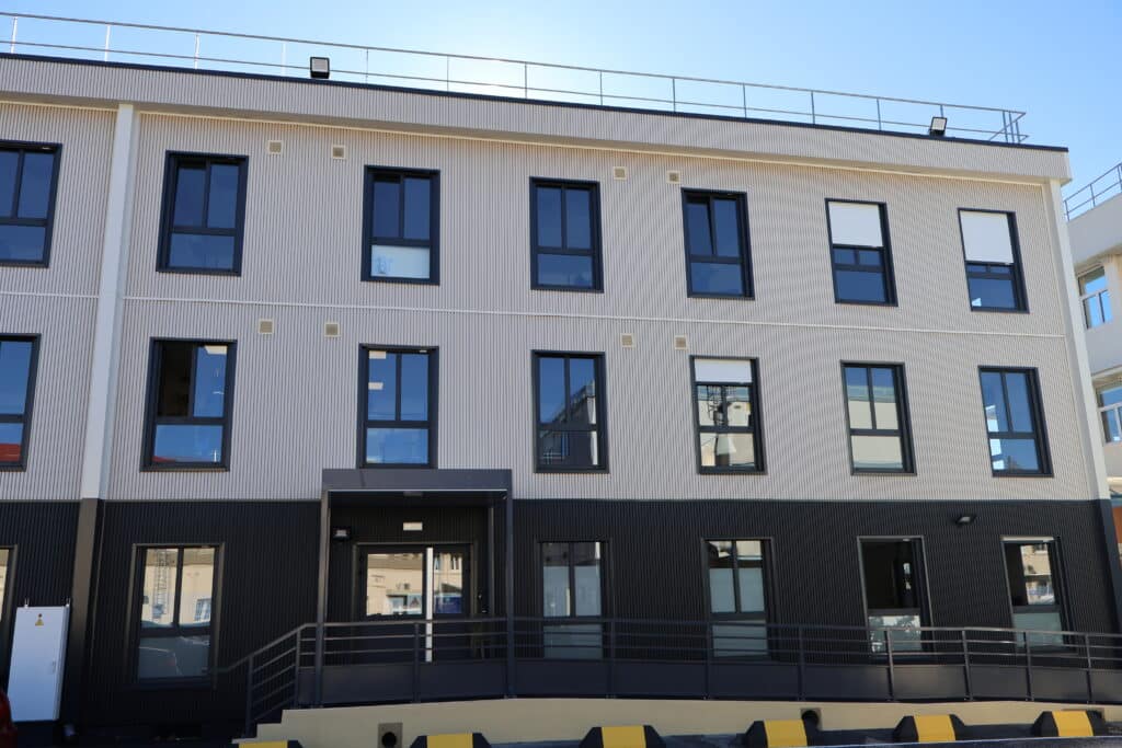 Façade d’un bâtiment modulaire en bois à deux étages avec bardage vertical clair et menuiseries noires